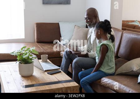 African American senior child sitting at home on brown sofa holding docs viewing laptop, copy space Stock Photo