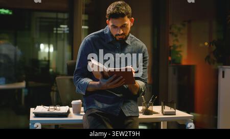 Serious concentrated Arabian business writing notes man in dark night evening office professional specialist with planner notebook Indian businessman Stock Photo