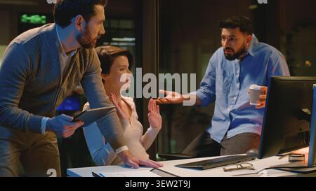 Three business workers team group of employers arguing talking using computer and digital tablet managers angry communicating at dark night office Stock Photo