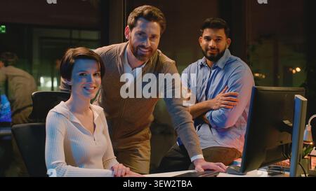 Three diversity international business managers smiling looking at camera at dark office happy positive men with woman group of workers corporate team Stock Photo