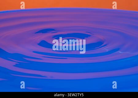 Concentric circles on the surface of the water created by the fall of a drop, with a prevalence of blue and orange colors Stock Photo
