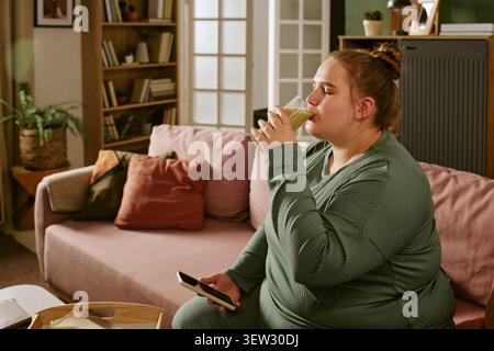Plus Size Woman Drinking Smoothie While Using Smartphone at Home Stock Photo