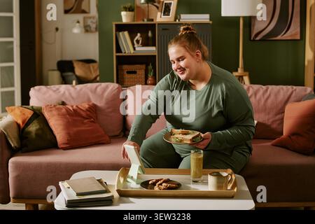 Plus Size Woman Having Meal during Video Call at Home for Remote Socializing Stock Photo