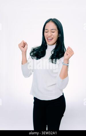 Excited Asian Woman Celebrating Success with Clenched Fists on White Background Stock Photo