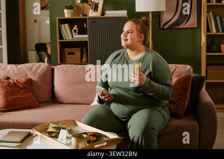 Plus Size Woman Relaxing with Smoothie and Smartphone at Home Stock Photo