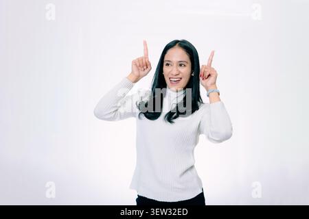 Cheerful Asian Woman Smiling and Pointing Up with Both Index Fingers Stock Photo