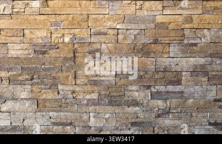 Wall made of reconstructed strips stone with warm tones ranging from beige to ochre, all the way to gray and reddish shades. Rustic coating Stock Photo