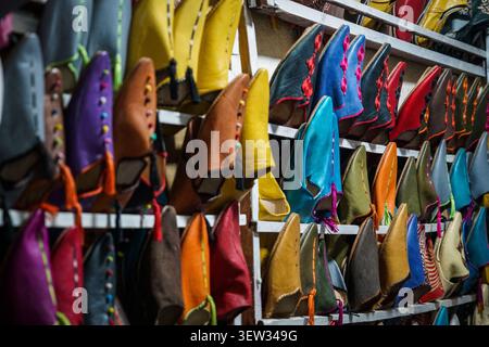 Many pairs of vibrant leather babouches, traditional Moroccan slippers, are arranged on shelves in a market stall. These slippers are handmade and are Stock Photo