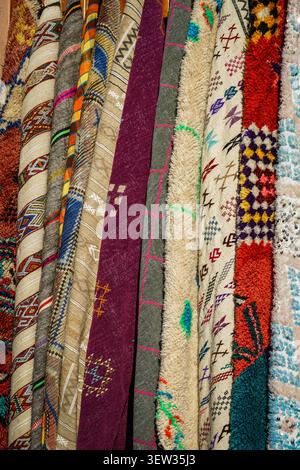A collection of rolled Moroccan rugs and blankets with various patterns and textures are arranged vertically in a marketplace. This image is suitable Stock Photo
