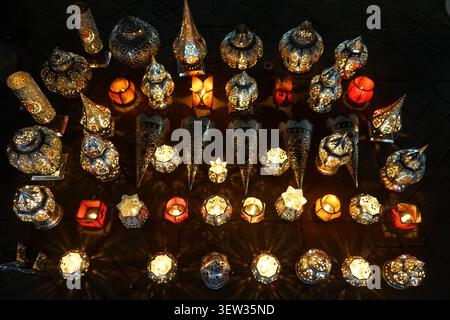 An overhead shot displays a variety of traditional Moroccan metal lanterns and lamps illuminated from within, casting intricate light patterns onto th Stock Photo
