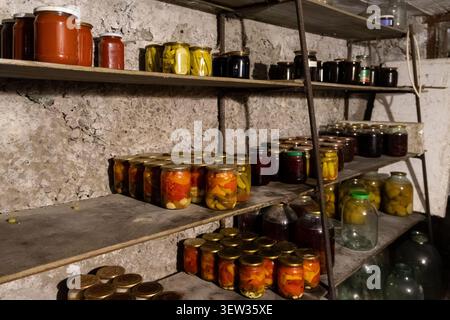 Rows of preserved vegetables and fruits stored in sealed glass containers on dark shelves highlight self-sufficiency, sustainable home canning, and ru Stock Photo