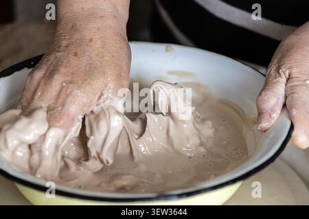 Mature hands mix a lively active sourdough starter within a rustic metal bowl, capturing the authentic process of artisanal fermentation for tradition Stock Photo