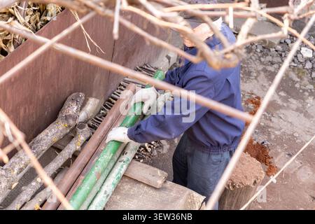A mature person in work clothes organizes heavy steel materials during a garden renovation, emphasizing the effort, endurance, and practical craftsman Stock Photo