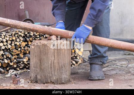 A person in protective gear steadies a heavy metal cylinder on a wooden block before using power tools, showcasing industrial craftsmanship and mainte Stock Photo