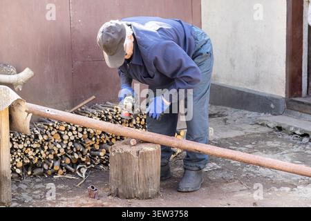 A skilled craftsman cuts a metal pipe with a power tool on a wooden block at a rural home site, demonstrating professional repair work, technical skil Stock Photo