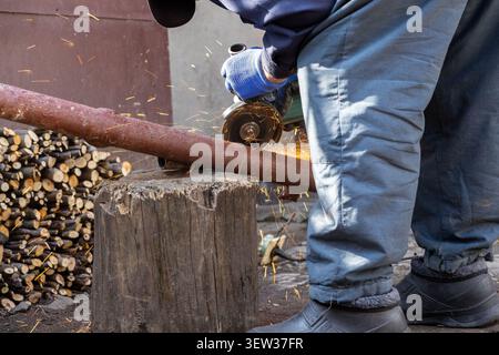 A person cuts an iron tube with a portable disc grinder outdoors, where flying metallic sparks highlight the intensive process of home maintenance, pr Stock Photo