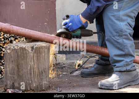 Hand wearing a protective glove holding a power tool to slice through steel pipe, illustrating diligent manual labor, industrial maintenance, and DIY Stock Photo