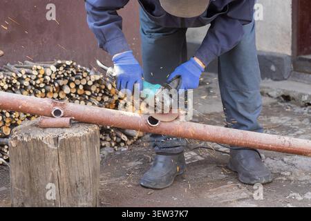 A skilled craftsman wearing protective gloves cuts steel piping with a powerful hand tool, demonstrating mechanical repair expertise within a rustic e Stock Photo