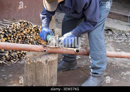 A skilled person in protective gear cuts rusty steel tubing with a handheld electric tool, highlighting industrial craftsmanship, metalwork precision, Stock Photo