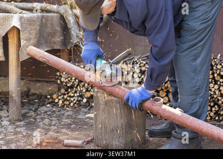 A skilled person cuts a rusted steel tube with a handheld power tool while sparks fly in an outdoor industrial setting to represent renovation, metal Stock Photo