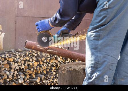 A person in protective gloves uses an angle grinder to cut through a steel tube as orange sparks fly, emphasizing industrial maintenance, DIY home rep Stock Photo
