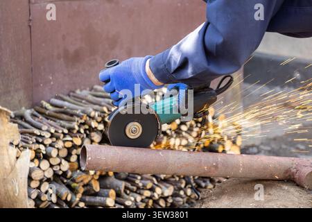 A close view of gloved hands operating a power tool to slice a rusty steel pipe, creating bright sparks that demonstrate high precision and effort in Stock Photo