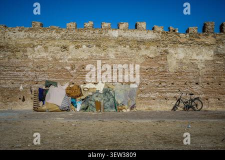 A weathered ancient city wall with battlements forms the background to a makeshift shelter constructed from various materials and a bicycle parked nea Stock Photo