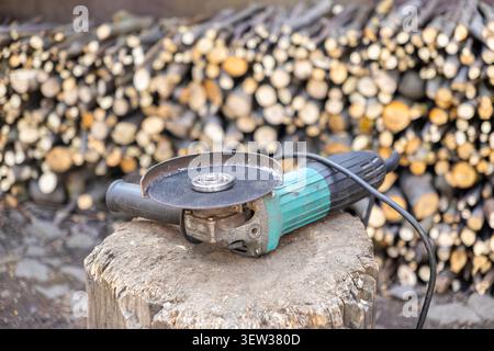 A powerful corded angle grinder sits on a log stump outdoors to showcase essential maintenance tools used for home improvement projects and forestry w Stock Photo