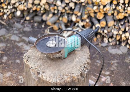 Professional power tool positioned on a tree stump in front of firewood, illustrating labor readiness, renovation progress, and the rugged utility of Stock Photo