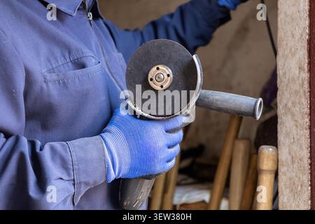 A technician in workwear uses an electric angle grinder for metal grinding tasks, demonstrating the careful handling of power tools for manual labor a Stock Photo