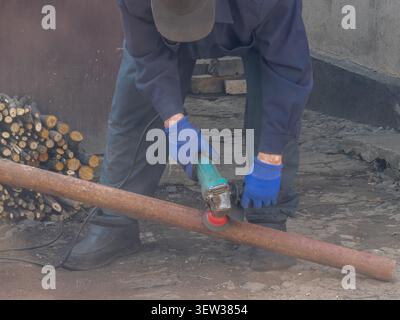 Person grinding an old metal tube with a power tool to remove surface corrosion at a yard, demonstrating skilled trade craftsmanship for renovation or Stock Photo