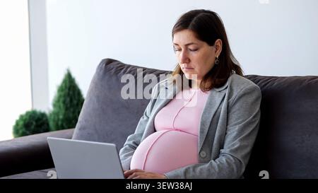 Pregnant woman working from home on laptop Stock Photo