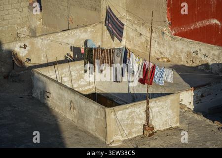 An overhead view of a weathered rooftop shows a clothesline laden with various garments drying in the sun. A ginger and white cat sleeps peacefully in Stock Photo
