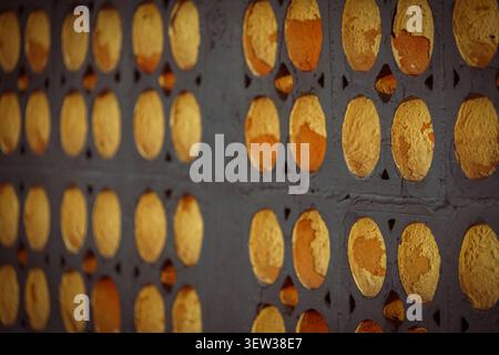 This close-up abstract image features a repeating pattern of oval depressions on a dark gray textured wall. Many of the depressions are painted gold, Stock Photo
