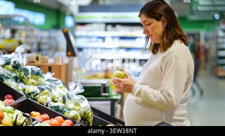 Pregnant woman choosing fresh fruit in supermarket produce section Stock Photo
