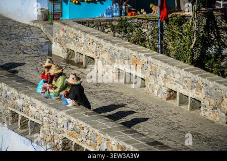 Chefchaouen, Morocco - 07 December 2017: Three women wearing colorful traditional straw hats with pom-poms are seated on a low stone wall next to a co Stock Photo