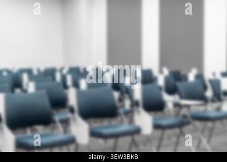 Blurred empty lecture hall with rows of blue ergonomic chairs, folding desks. Academic seminar, corporate training, university education background. Stock Photo