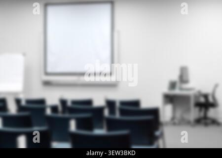Blurred empty university lecture hall or classroom blue chairs, projector screen, flipchart. Academic presentation, educational seminar background. Stock Photo