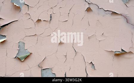 Close up of a weathered deteriorating tan painted wall surface with cracked peeling paint revealing concrete underneath Stock Photo