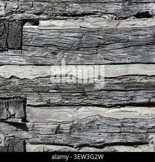 Close up of aged log cabin flat logs and chinking surface with dry cracked rough wood, rusty nails, porous chipped chink Stock Photo