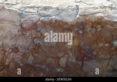 Close up of the weathered surface of a large stone with light tan color at the top, dark brown at the bottom, porous uneven texture Stock Photo