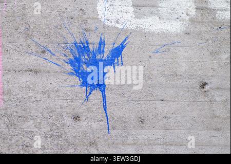Rough gray concrete wall featuring a vibrant blue paint splatter and faint marks. Stock Photo