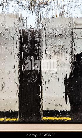 Close-up abstract view of rain running down a train window, creating streaks and droplets on the glass Stock Photo