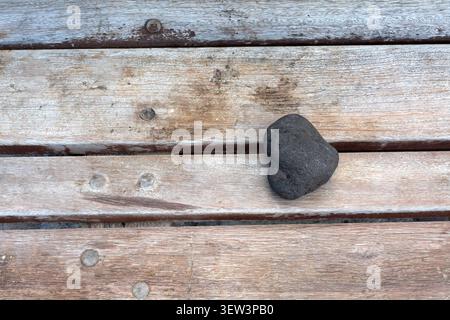 High angle view of a small dark porous stone positioned on weathered wooden boards, creating a simple and natural abstract texture concept with copy s Stock Photo