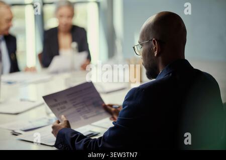 Black businessman reviewing documents during oil industry meeting with colleagues, discussing contracts and strategy. Useful for energy sector leadership, corporate planning, investment Stock Photo