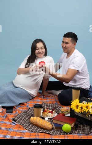 Romantic couple sitting on a picnic blanket and holding a red heart sign Stock Photo