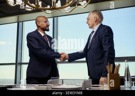 Low angle view of middle aged businessmen shaking hands during oil industry meeting, signaling partnership and negotiation. Ideal for energy sector leadership or B2B deal marketing Stock Photo