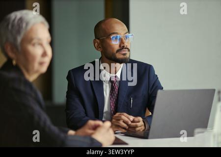 Medium shot of South Asian businessman discussing oil industry strategy during meeting with senior businesswoman, using laptop. Ideal for energy sector leadership, planning, partnership Stock Photo