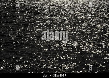 A high-angle abstract view captures countless specks of sunlight reflecting intensely off the dark, rippling surface of a water body in Auckland, New Stock Photo