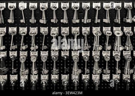 This black and white image features a detailed close-up of numerous vintage metal keys, neatly arranged in rows on a dark, perforated display board. E Stock Photo